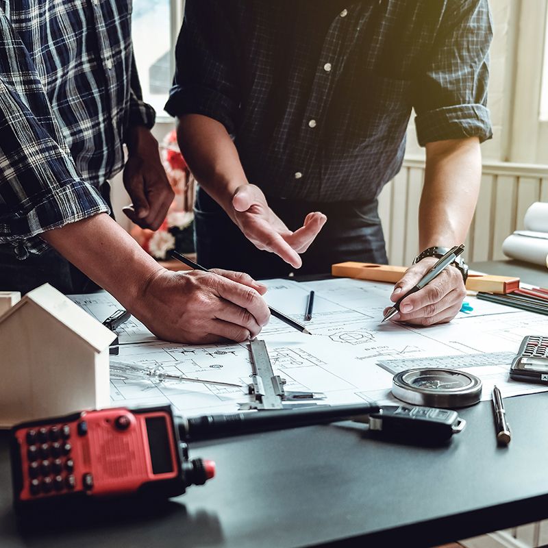 Zwei Männer analysieren einen Bauplan an einem Tisch und tauschen Ideen zur Umsetzung aus
